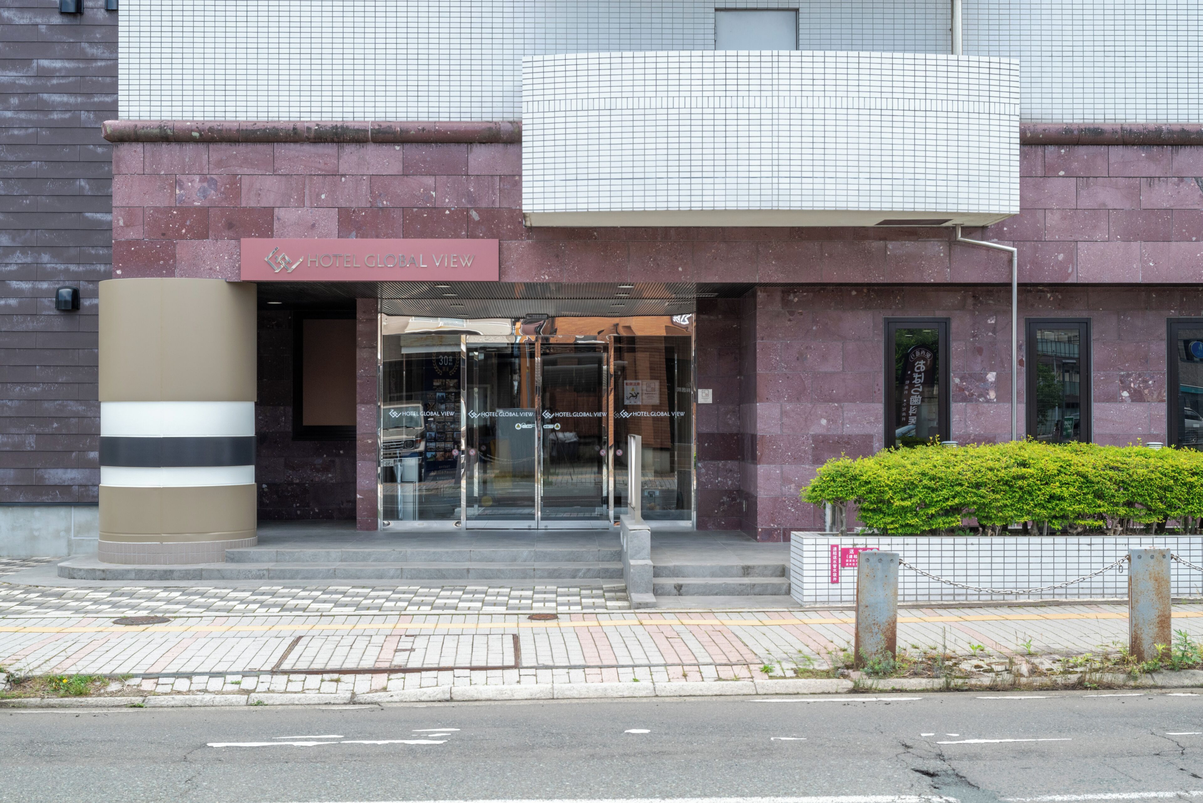 A hotel entrance with a glass door, a sign reading 'HOTEL GLOBAL VIEW,' and a small garden area.