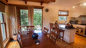 Een gezellige keuken met houten meubels, een eethoek met tafel en stoelen, en uitzicht op groen buiten.