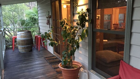 A porch with a wooden floor, a potted plant, a red stool, and a barrel.