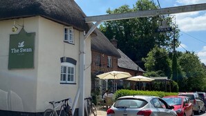 A building with a sign reading "The Swan" and a thatched roof.
