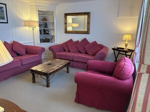 A living room with a sofa set, a wooden coffee table, a bookshelf, a mirror, and a lamp.