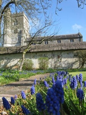 A historic building with a tower and thatched roof, surrounded by a garden with blue flowers. - Stunning 3 bed/3 bath cottage nr Stonehenge & Bath, Sleeps 6. Walled garden (Pewsey)