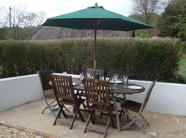 An outdoor patio with a round table and four chairs, a green umbrella, and a thatched roof structure in the background. - Stunning 3 bed/3 bath cottage nr Stonehenge & Bath, Sleeps 6. Walled garden (Pewsey)