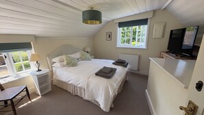 A bedroom with a bed, a desk with a chair, a television, and a window with blinds.