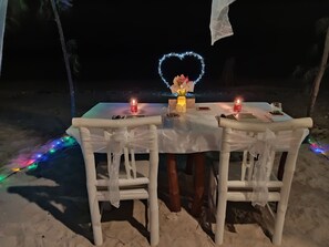 An outdoor dining setup with a table and chairs, candles, and a decorative heart-shaped light. - Villa Coral Flora (Gili Trawangan)