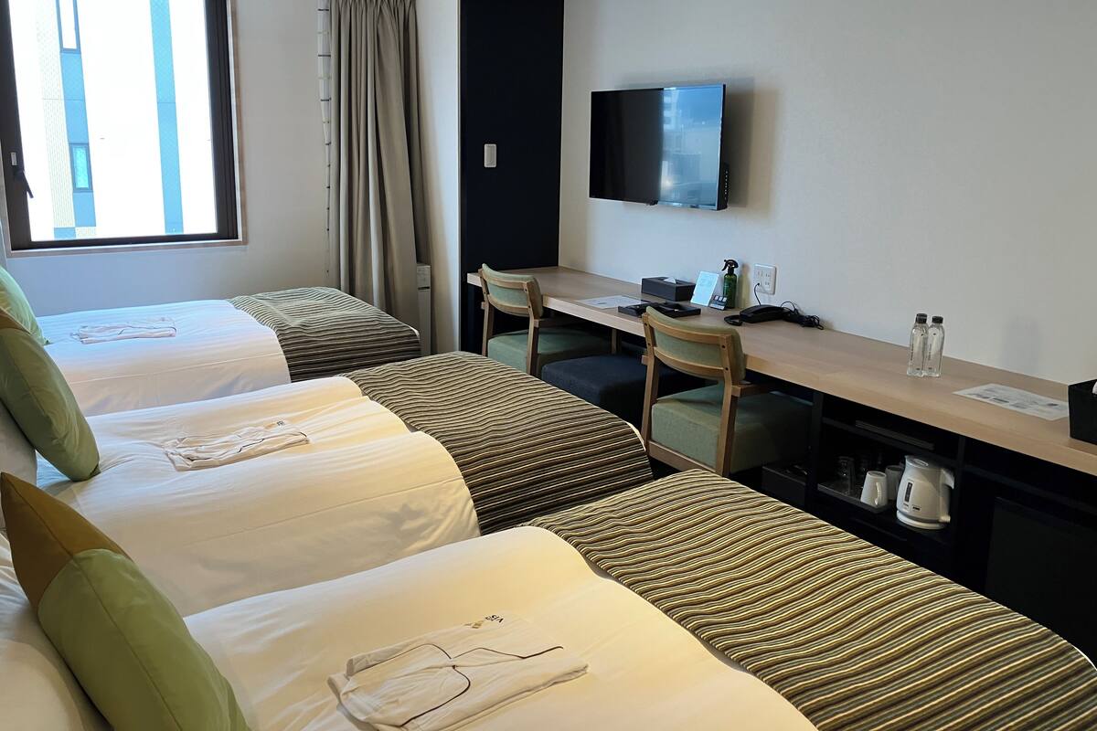 A hotel room with two single beds, a desk with a chair, a television, and a window with curtains.