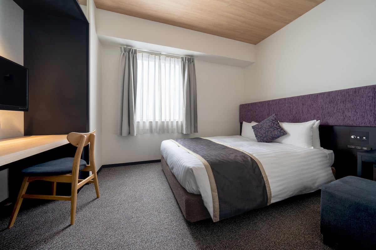 A hotel room with a bed, a desk, a chair, and a television.