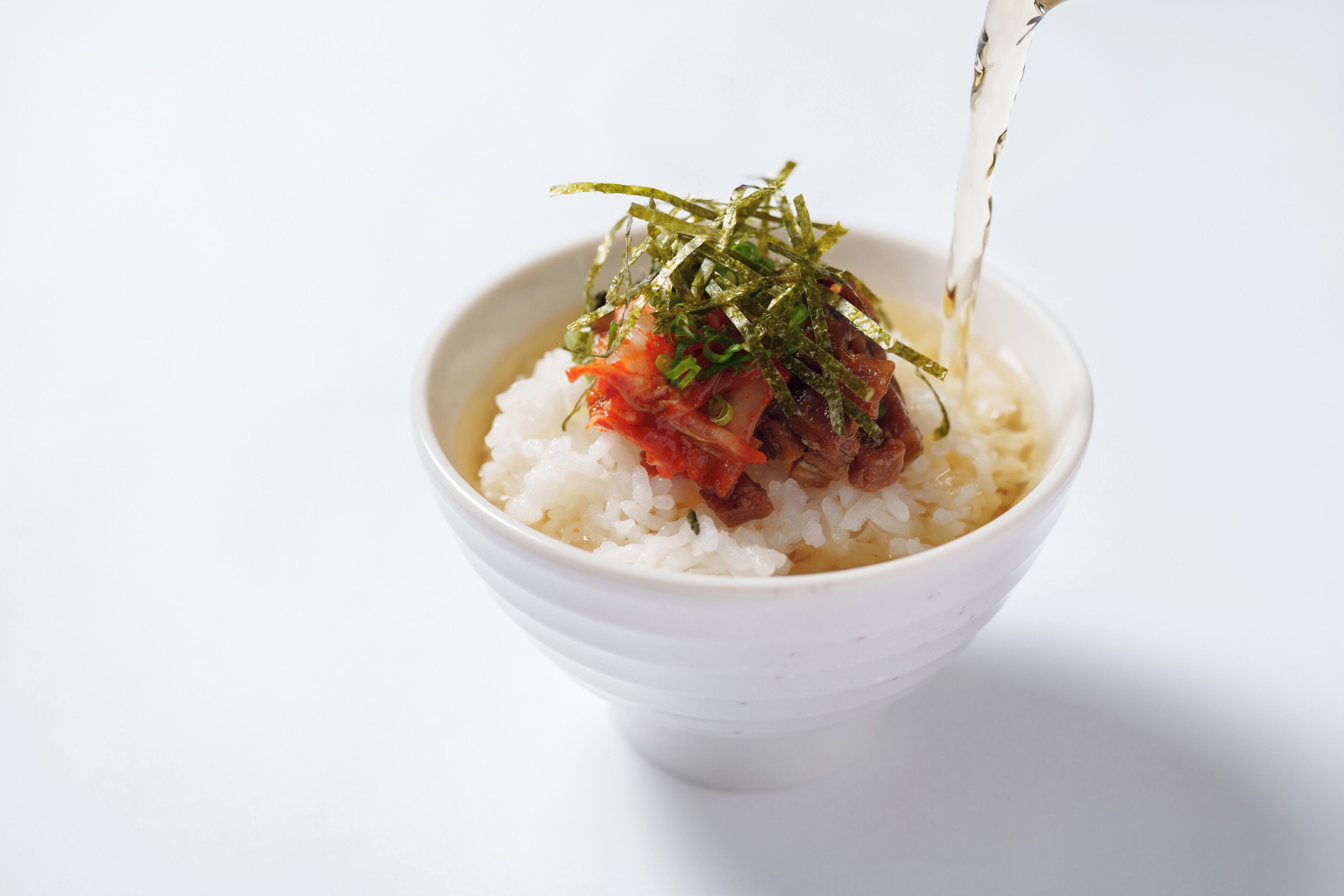 A bowl of rice topped with a sauce and seaweed garnish.