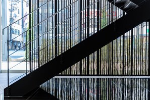 A modern staircase with metal railings and a glass barrier, leading to an outdoor area with a view of the cityscape. - Hotel Vista Hiroshima (Hiroshima)