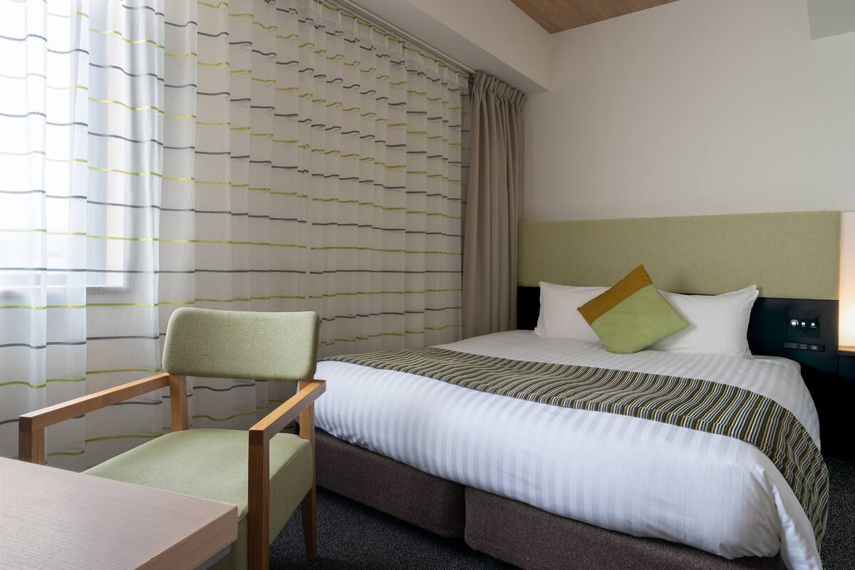 A hotel room with a bed, a chair, a table, and a curtain with a striped pattern.