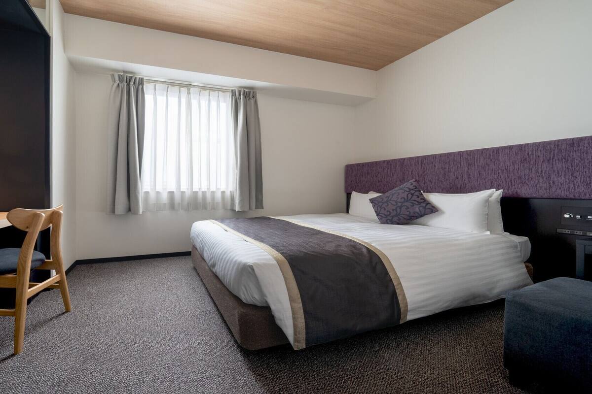 A hotel room with a bed, a desk, a chair, a television, and a window with curtains.