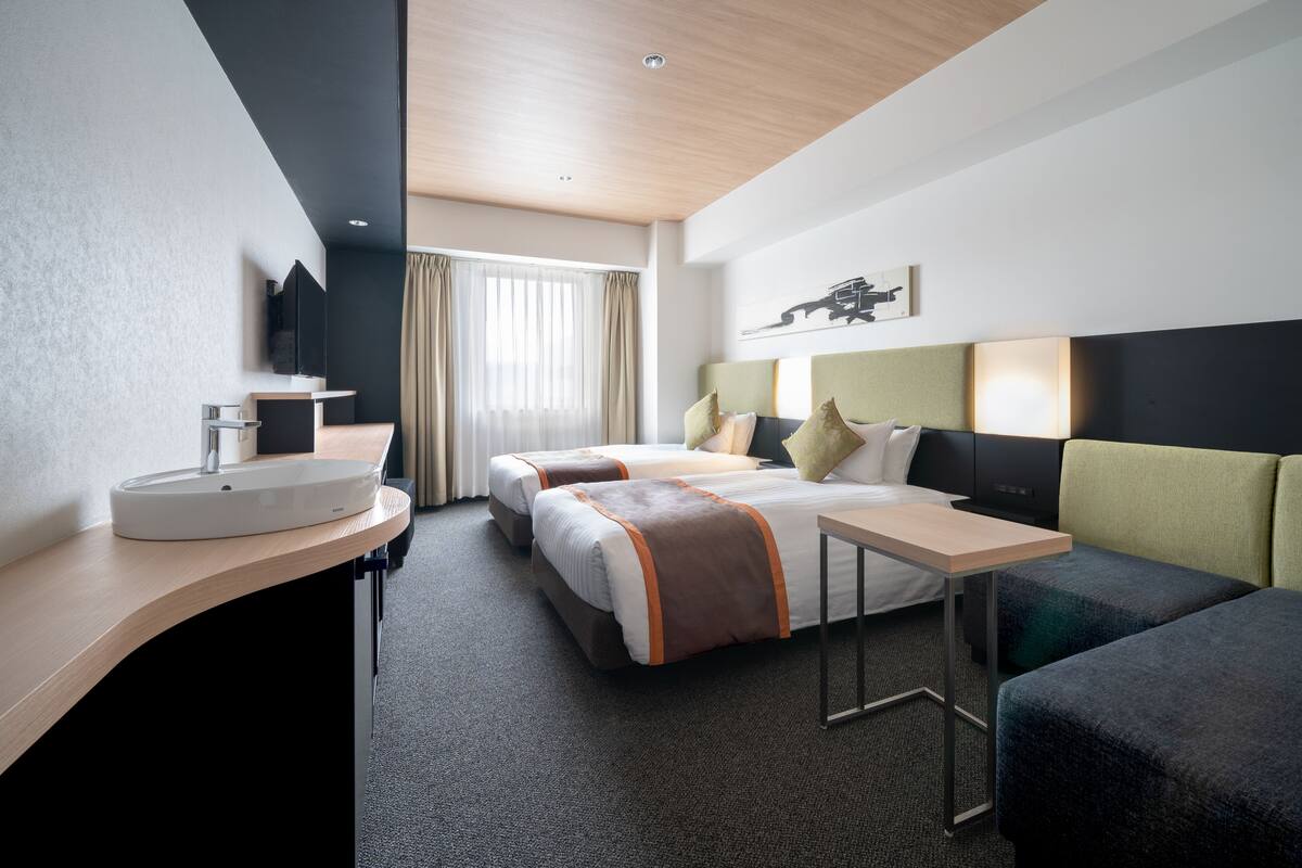 A hotel room with two beds, a desk, a sink, and a television.