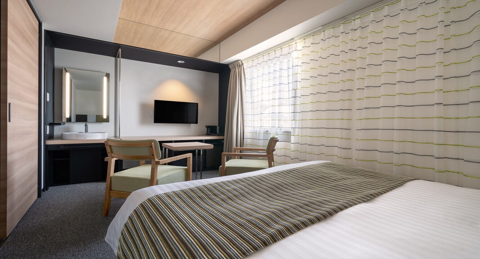 Ein Hotelzimmer mit einem Bett, einem Schreibtisch mit Stuhl, einem Fernseher und einem Fenster mit Vorhängen.