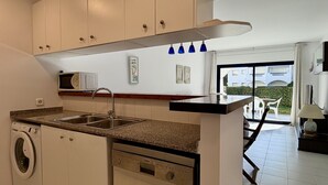 Een moderne keuken met een ingebouwde wasmachine, een spoelbak en een magnetron. Er is een raam met uitzicht op een gebouw en een balkon met stoelen.
