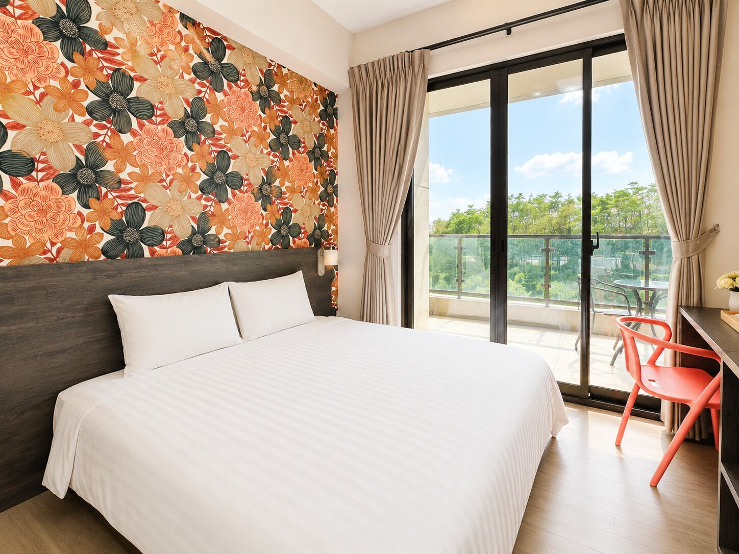 A hotel room with a large bed, a balcony with a view, and a small table with a chair.