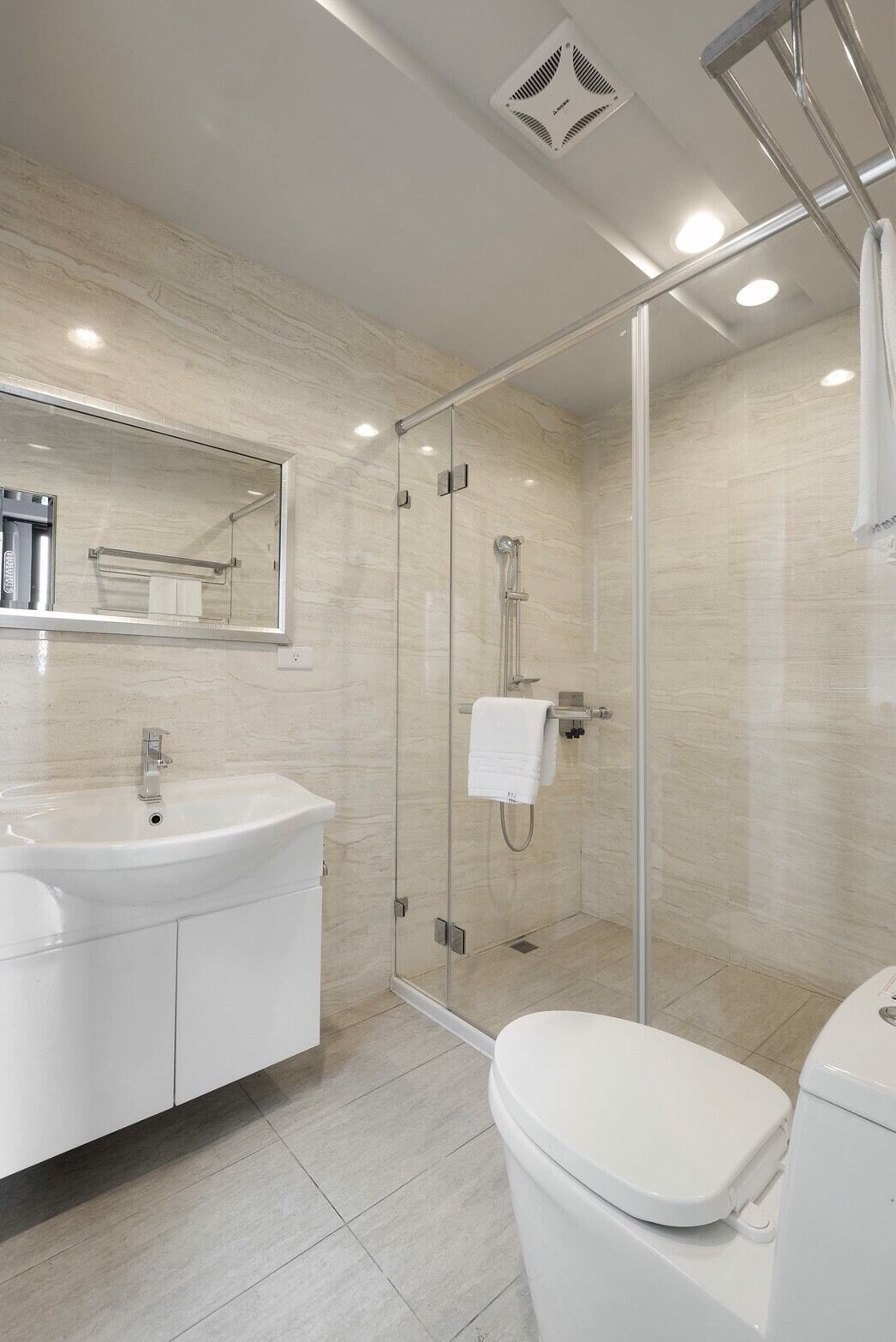 Un baño moderno con ducha envuelta en vidrio, un lavamanos blanco y un inodoro.