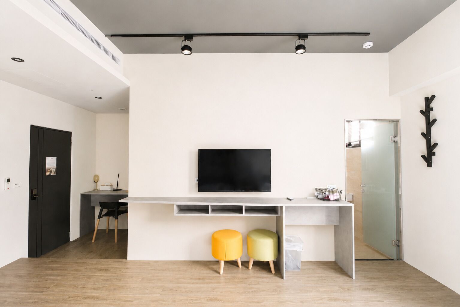 A modern living room with a flat-screen TV, a desk, and two colorful ottomans.