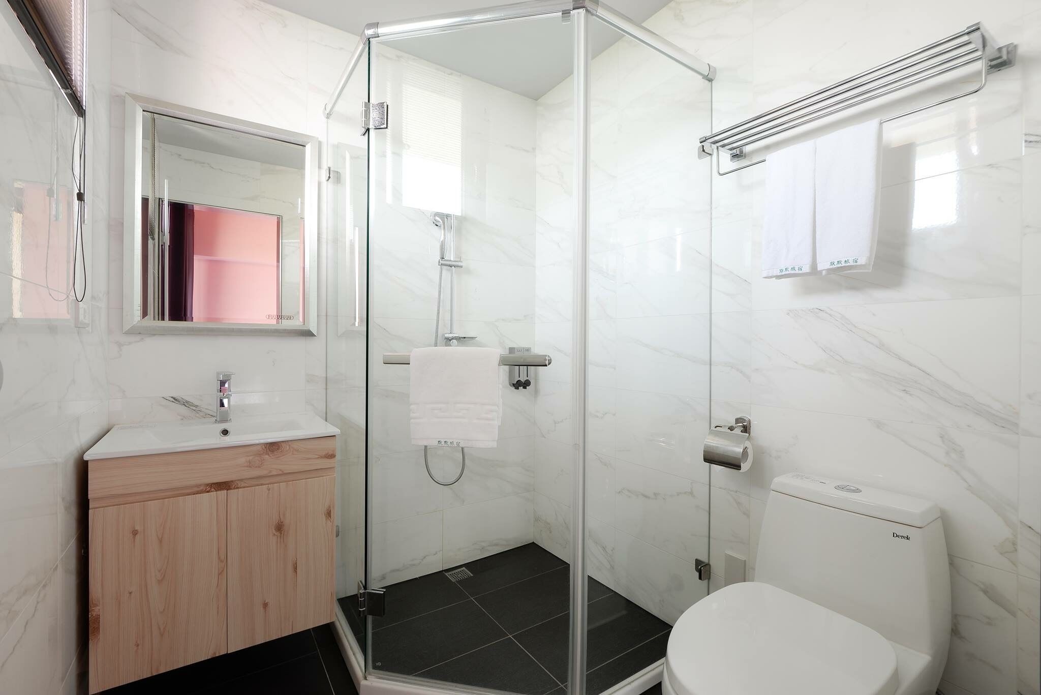 Een moderne badkamer met een douchecabine van glas, een wit wastafelmeubel met een houten kastje, en een toilet.