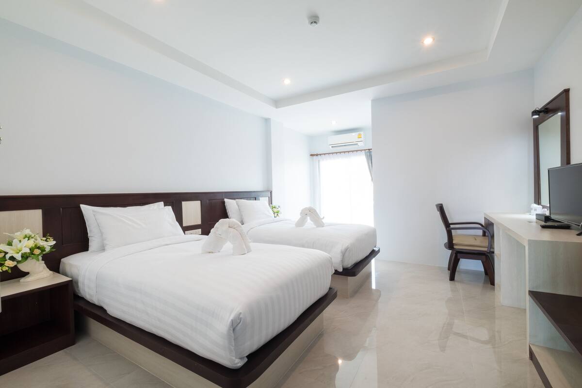 Habitación de hotel con dos camas, un escritorio, una silla y un televisor.
