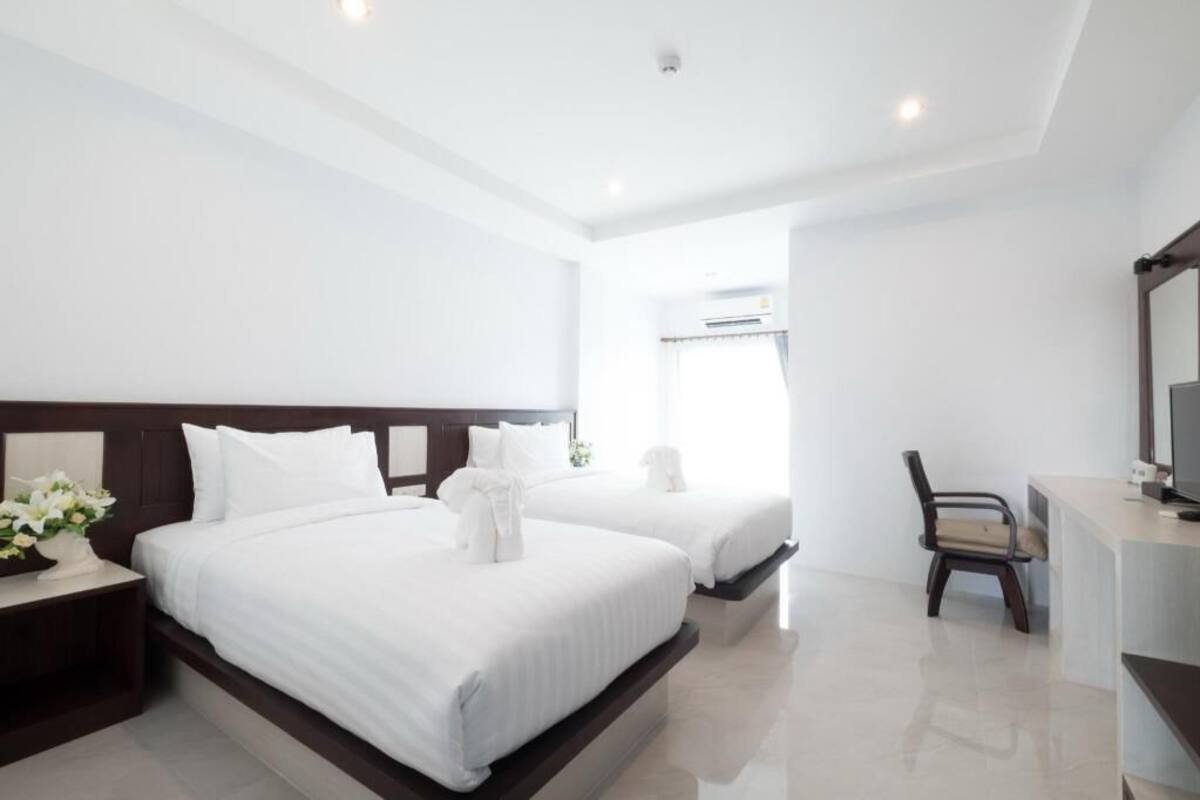 A hotel room with two beds, a desk, a chair, and a television.