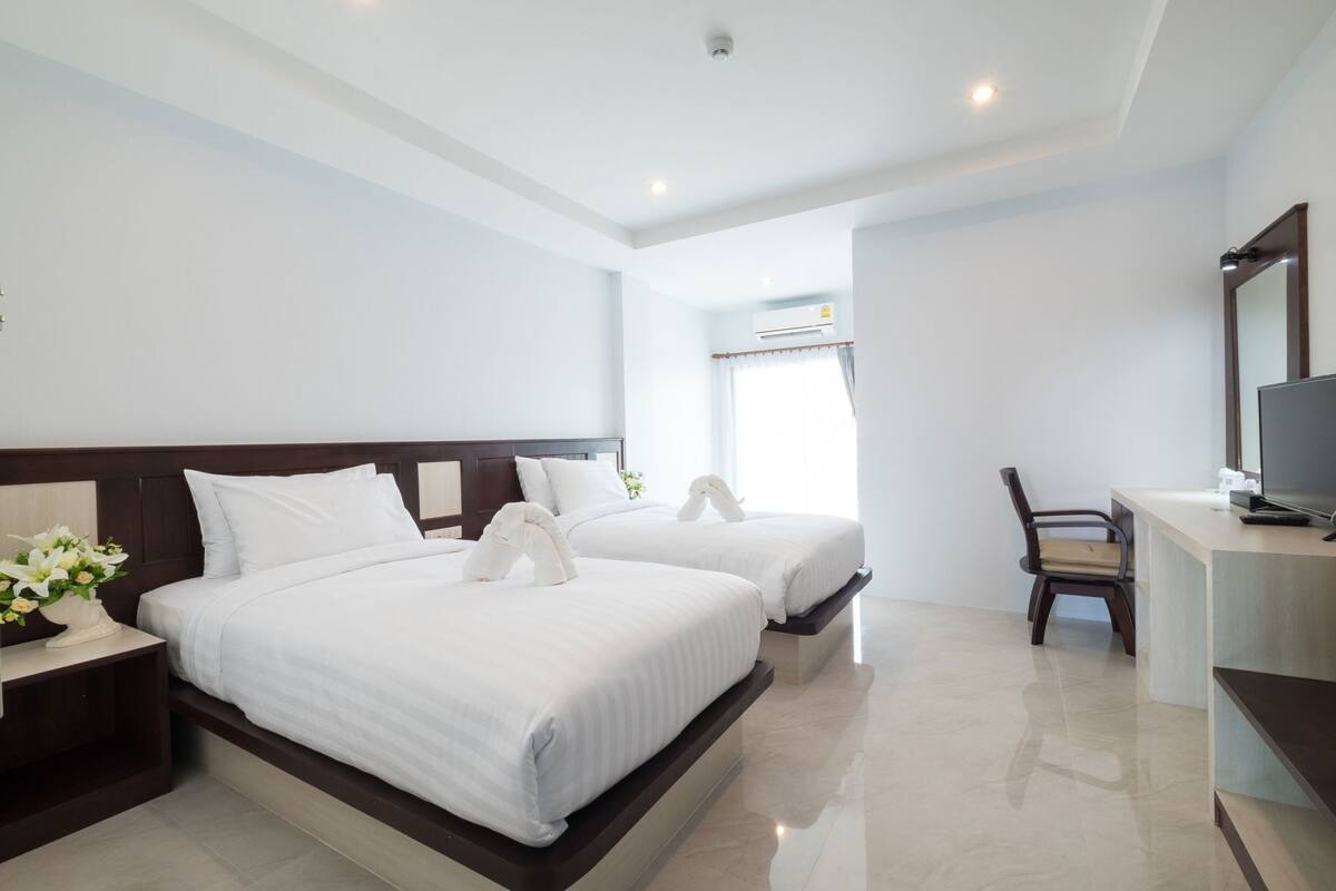 Habitación de hotel con dos camas, un escritorio, una silla, un televisor y una ventana con cortinas.