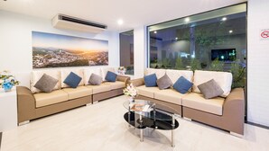 A modern hotel lobby with a beige sofa set, a glass coffee table, and a large window offering a city view. - Sita Krabi Hotel (Krabi)