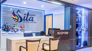A reception area with a marble counter, two chairs, a reception desk, and a decorative wall with the hotel name. - Sita Krabi Hotel (Krabi)