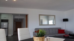 Una sala de estar moderna con un sofá gris, un sillón blanco, una mesa de centro, una lámpara de pie y un espejo en la pared.