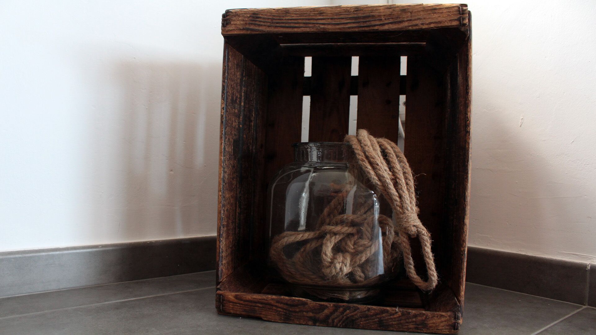A wooden crate with a glass bottle and a rope inside.