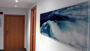 Un pasillo con una puerta de madera y un cuadro grande de una ola marina en la pared.