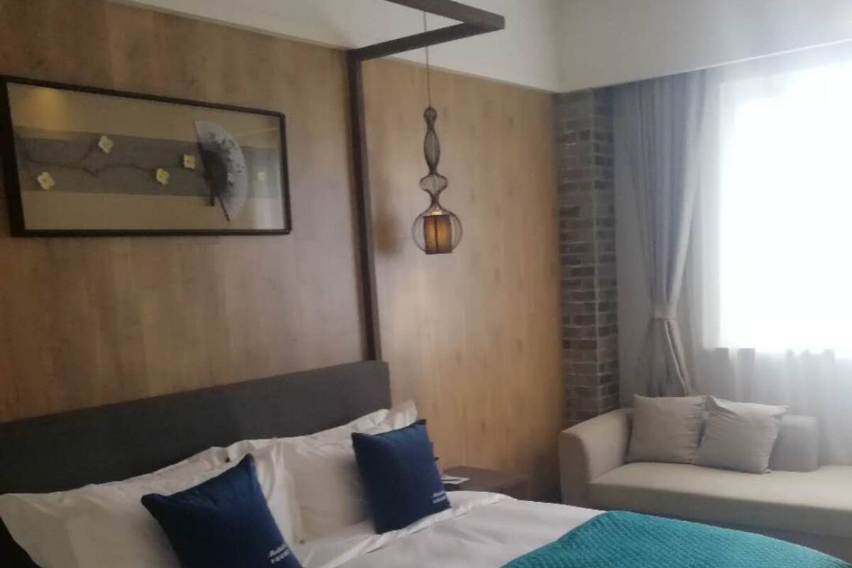 A hotel room with a large bed, a sofa, a hanging light fixture, and a window with curtains.