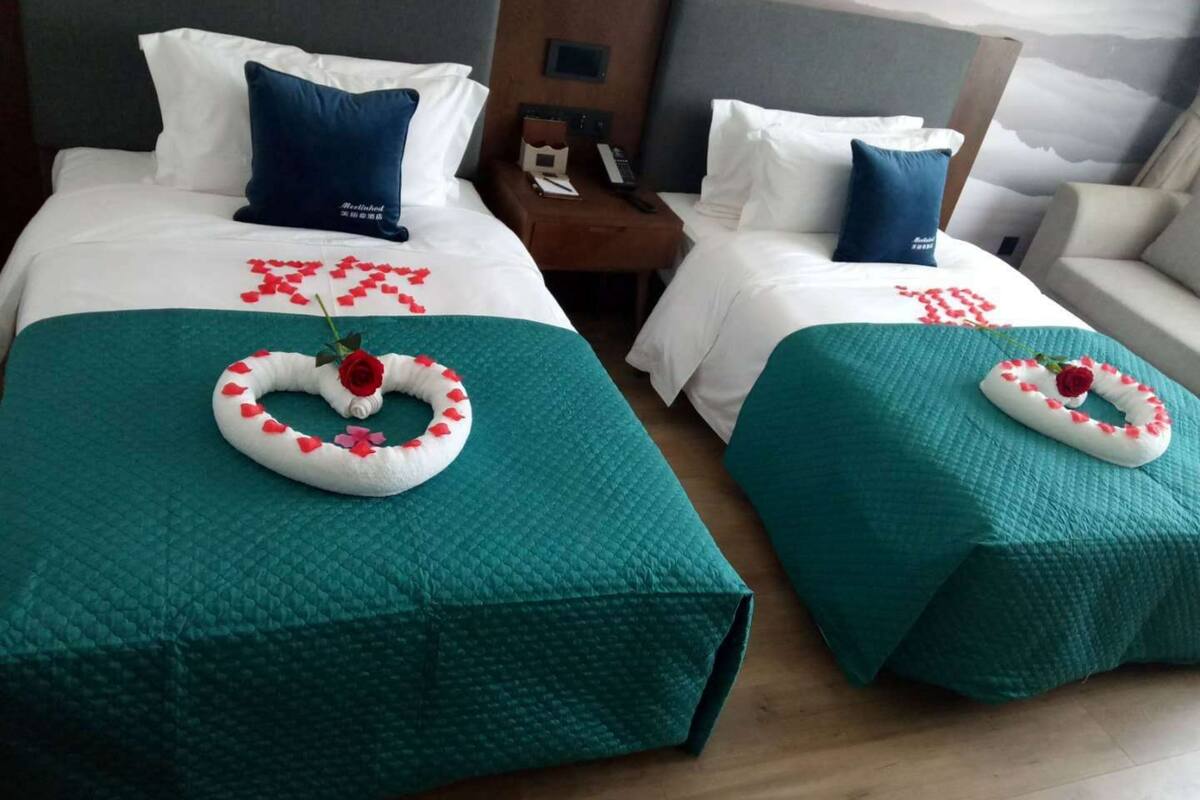 Two hotel beds with teal bedspreads, white linens, and decorative rose arrangements.