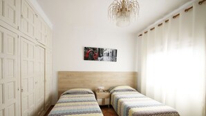 A room with two single beds, a wooden headboard, a nightstand, a lamp, and a wall-mounted picture.