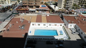 Un espace piscine aménagé sur le toit, avec une piscine, entouré de places de stationnement et de bâtiments.