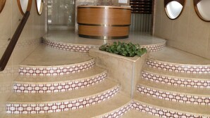 Un espace d’accueil avec un comptoir en bois, une plante au centre et un escalier dont les marches sont recouvertes de carreaux décoratifs.
