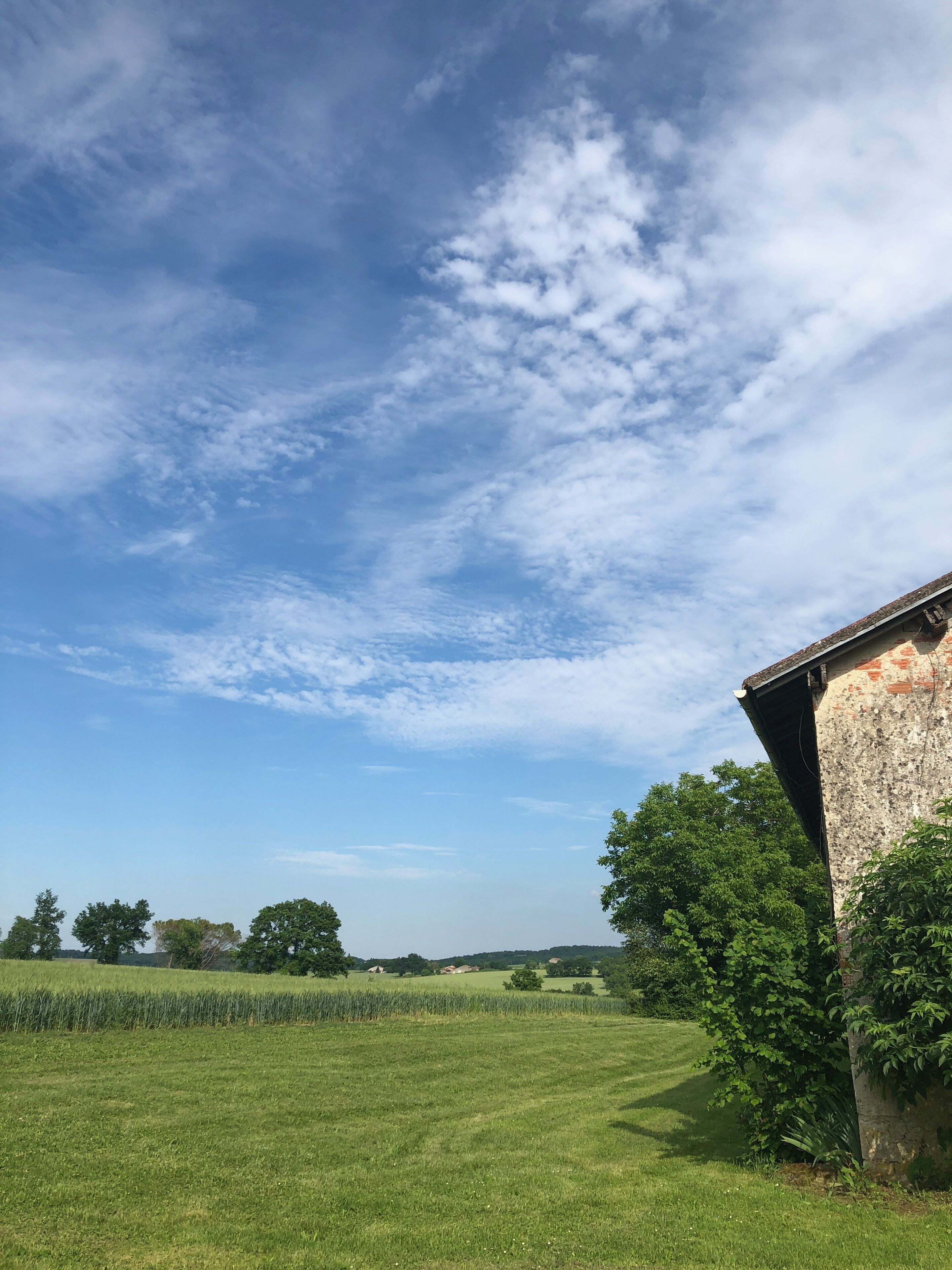 A rural landscape with a clear sky, green fields, and a stone building with a sloped roof.