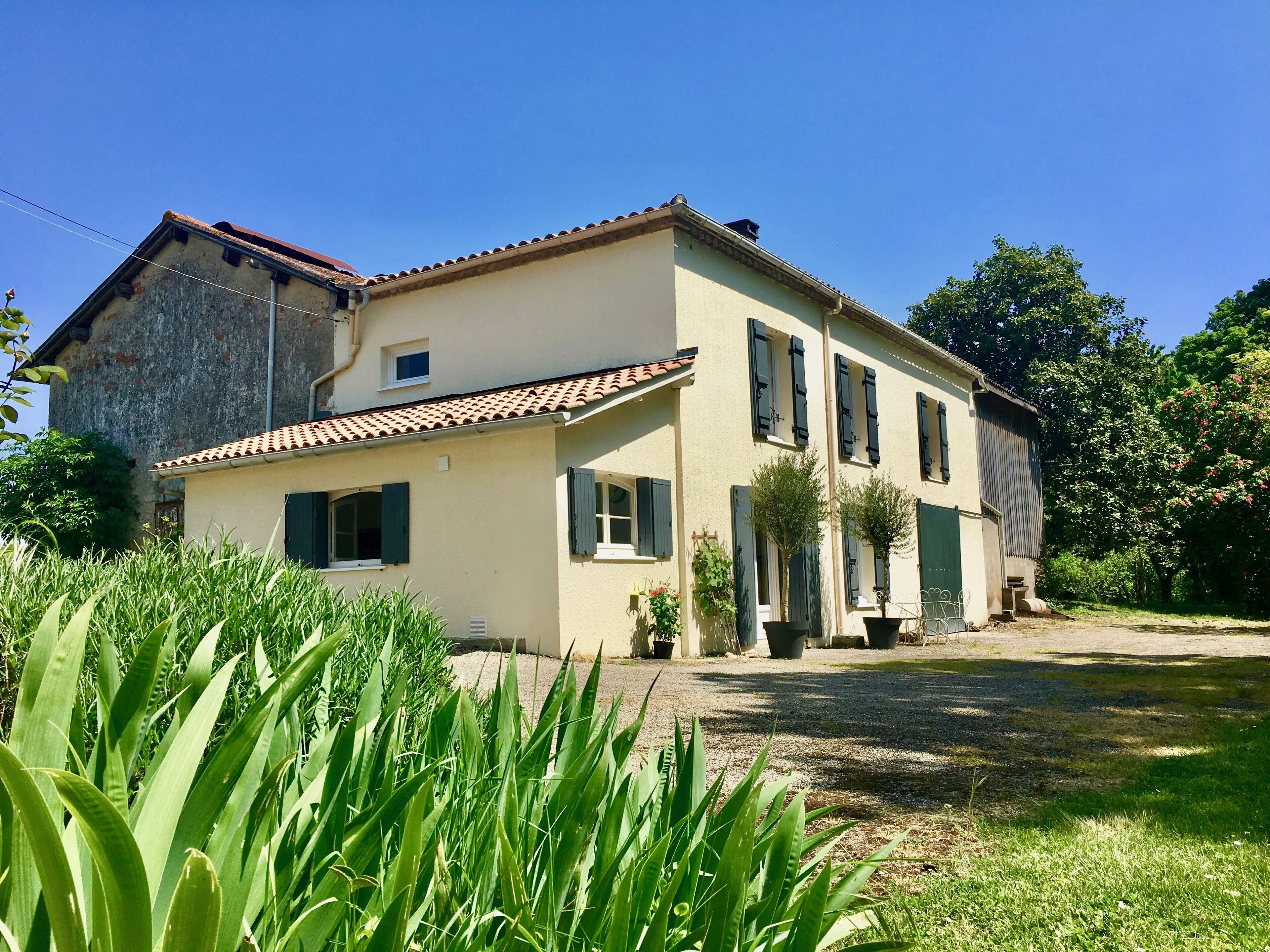 A two-story house with a tiled roof, a front porch, and potted plants.