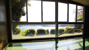 An indoor swimming pool with a view of a lake and greenery through large windows.