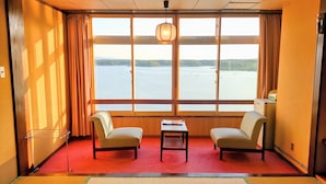 A room with two chairs, a small table, and a large window with a view of a body of water and hills.