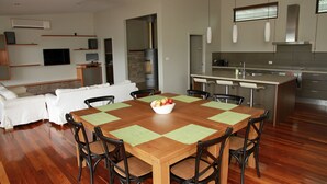 Una cocina moderna con una isla central, un comedor con mesa y sillas de madera, y una sala de estar con sofá y televisor.
