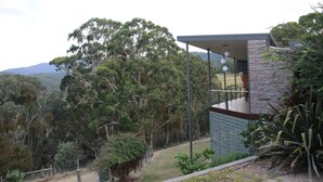 Una casa moderna con fachada de piedra, un balcón y vistas a un área boscosa.