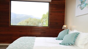Un dormitorio con un ventanal grande, una cama con ropa de cama blanca y vistas a un paisaje montañoso.