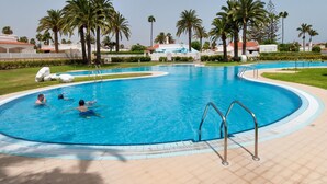 A large outdoor swimming pool with multiple lanes, surrounded by palm trees and a clear sky.