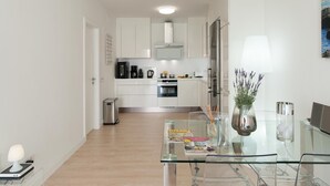 A modern kitchen with white cabinets, stainless steel appliances, and a glass dining table.