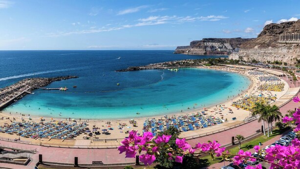 A coastal resort with a large sandy beach, a rocky cliff, and a marina.