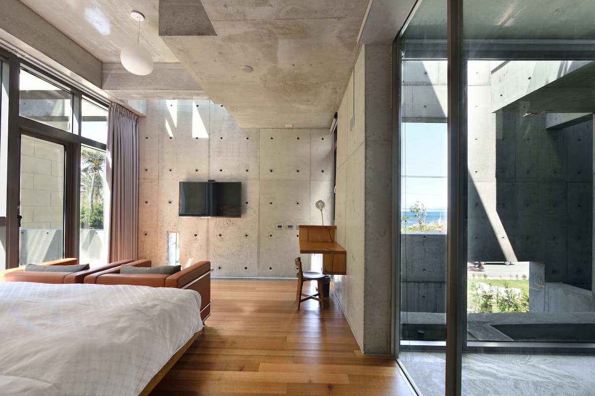 Camera da letto moderna con un letto grande, una scrivania e una sedia. C'è una TV montata a parete e una finestra che offre vista sull'esterno.