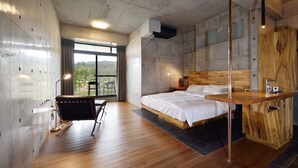 Un dormitorio moderno con una cama grande, un escritorio de madera, una silla y vistas a zonas verdes por la ventana.