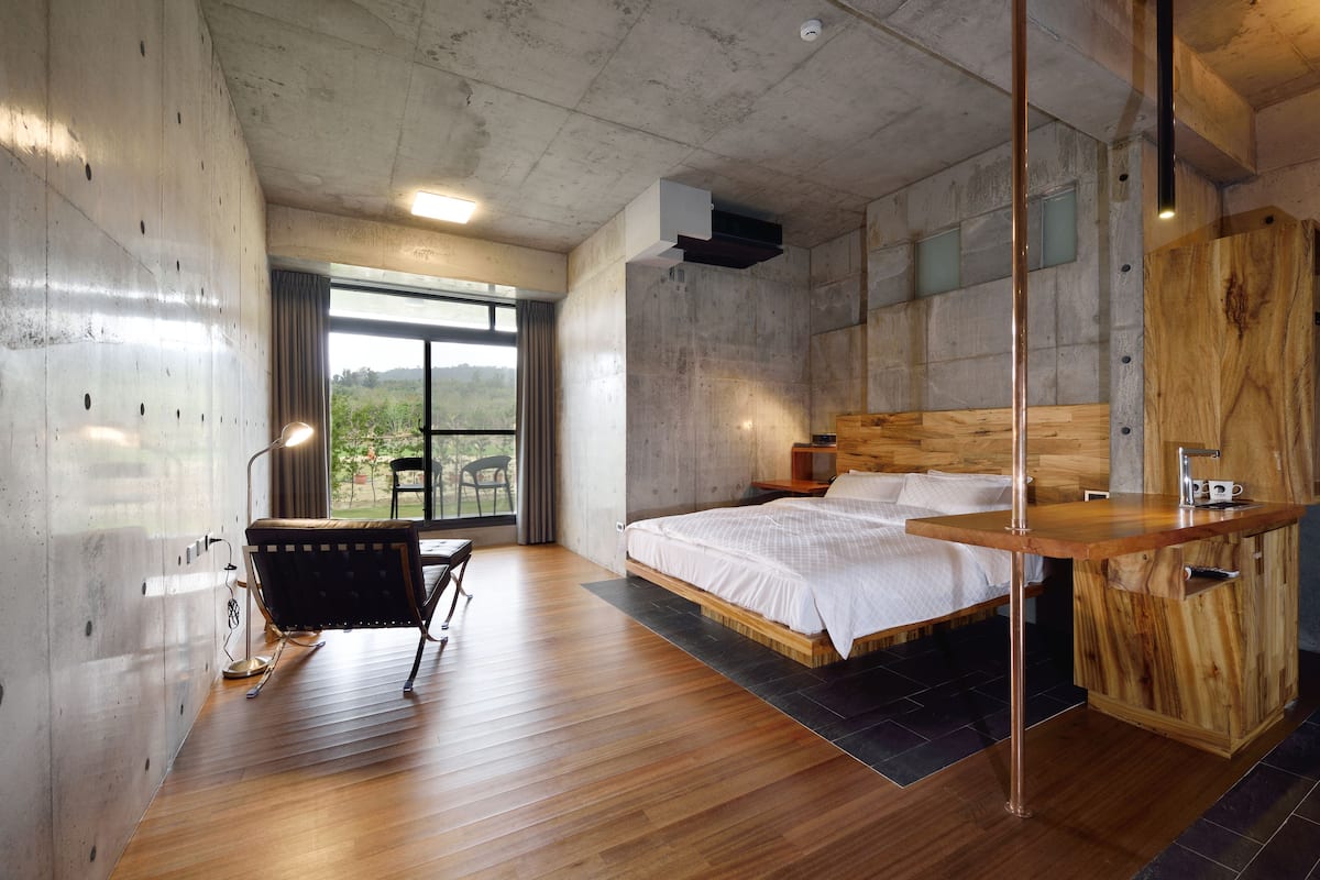 Camera moderna con un letto grande, una scrivania in legno, una sedia e vista sul verde dalla finestra.