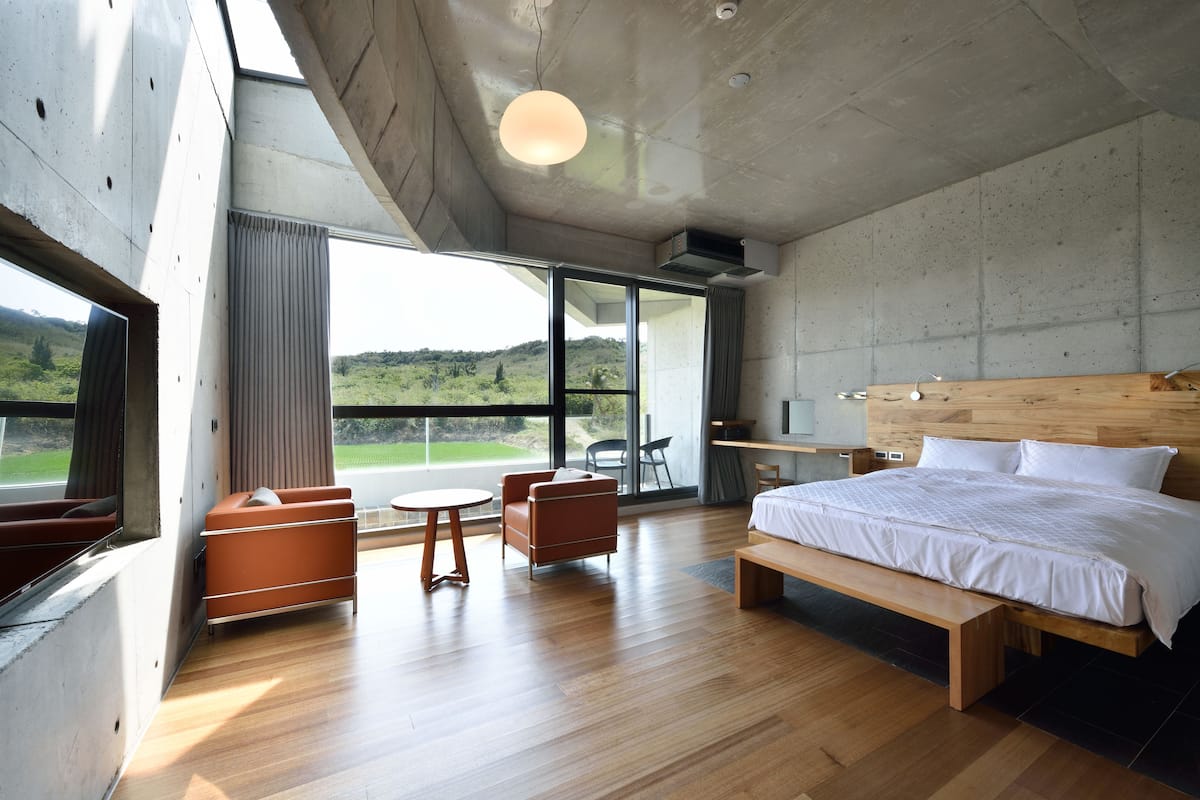 Camera da letto moderna con un letto grande, una testata in legno, una scrivania e vista sull'esterno.