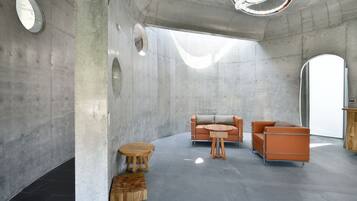 A modern interior with a concrete wall, a round wooden table, two orange sofas, and a round wooden stool.